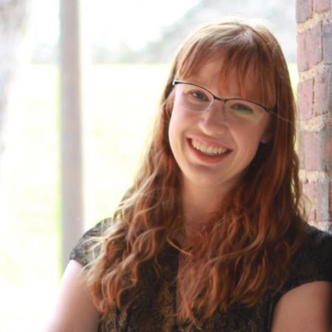 Erica headshot. Erica has long curly reddish blonde hair. She is wearing glasses and smiling. 