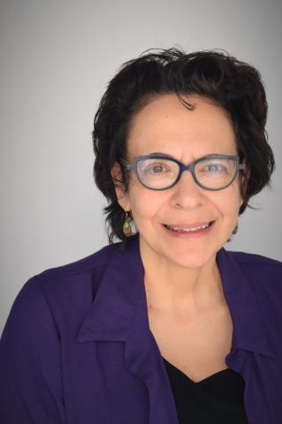 Headshot of Gigi. She has short brown hair. She is wearing glasses and is smiling. 