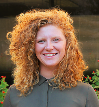 Picture of a woman with medium length red curly hair wearing a green blouse. 