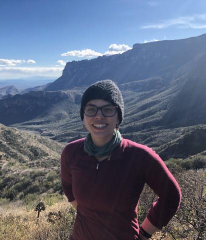 Photo of woman standing in the mountains, wearing a knit cap and a red sweater. 