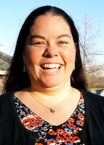 Picture of a woman with long, dark hair, wearing a flower blouse and a chain necklace. 