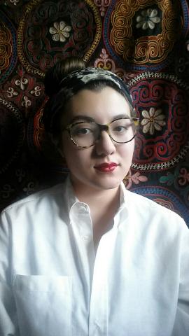 Picture of a woman with short black hair tied back in a bandana wearing glasses and a white shirt. 